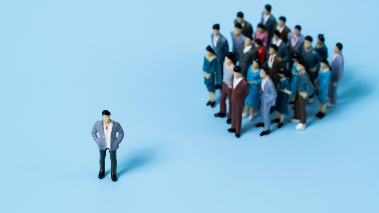 Businessman standing alone separated from a large group of people on a light blue background