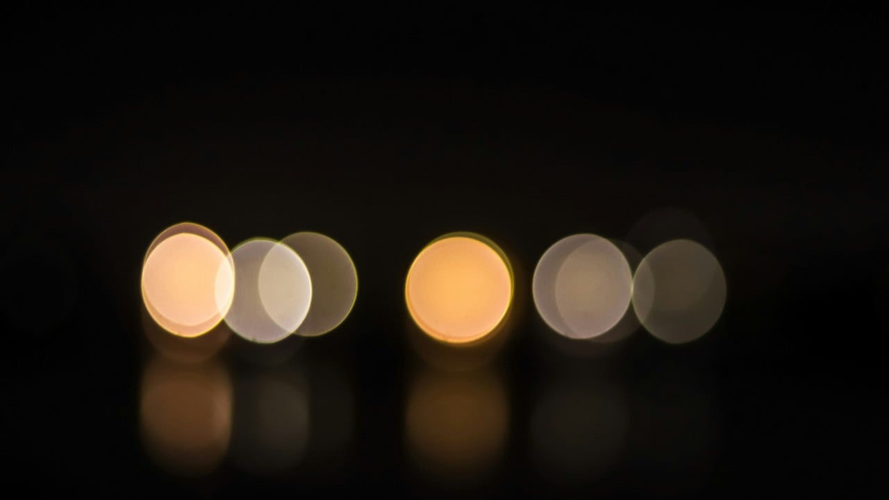 Six blurred circular light sources arranged in two groups on a dark background, showing warm and neutral tones with reflections.