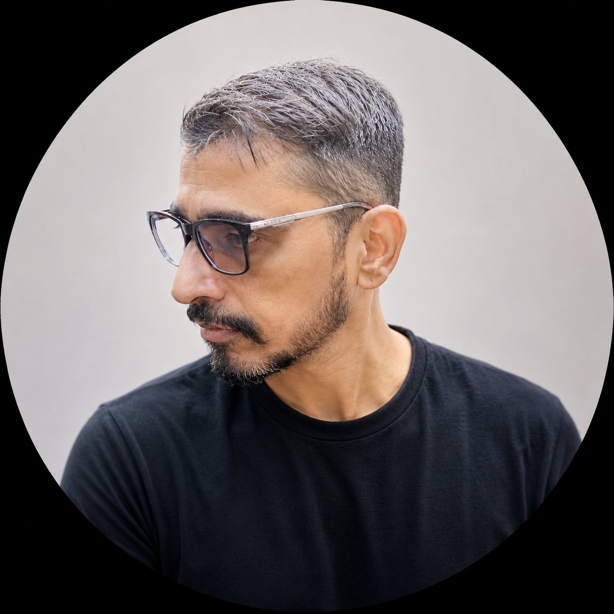 Man with gray hair and beard wearing sunglasses and black t-shirt, profile view against white circular background